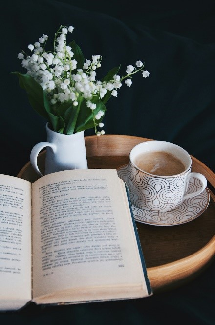 A cup of tea next to an open book and a bouquet of small white flowers